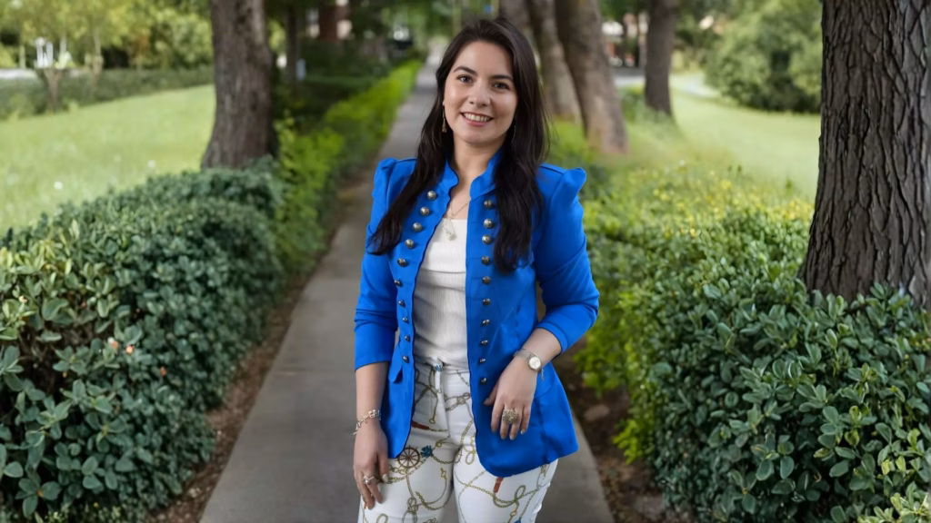 A photo of Luciana Ortega, the inaugural recipient of the Latin Music Educator Award, presented by the Latin Recording Academy and the
Latin GRAMMY Cultural Foundation. Ortega is smiling at the camera and wearing a blue blouse and a white shirt.