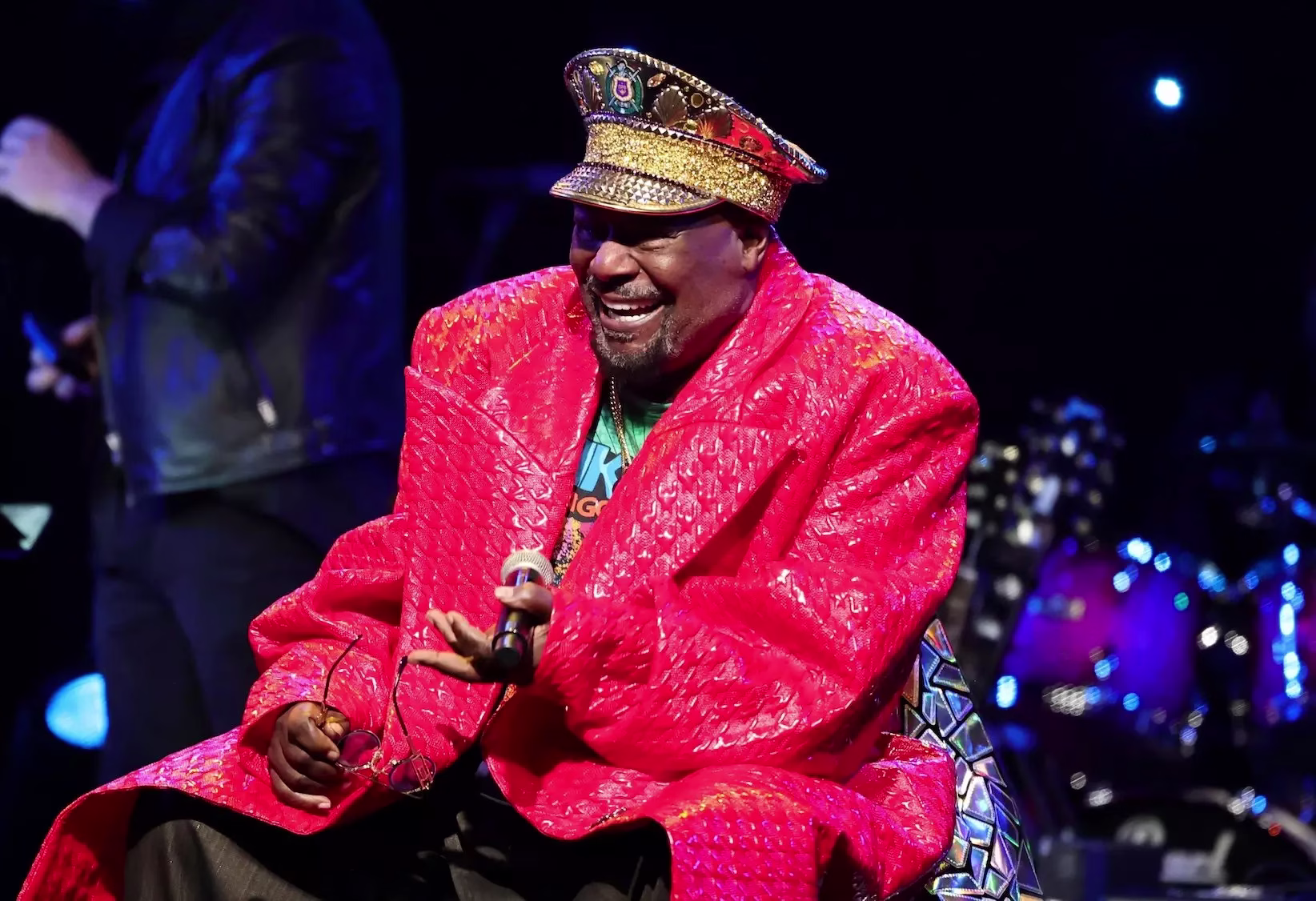 George Clinton with Funkadelic perform onstage during the 2026 Grammy Hall of Fame Gala on May 8, 2026, at The Beverly Hilton in Los Angeles. George Clinton is sitting on a chair while smiling and holiding a microphone and wearing a pink jacket and hat.