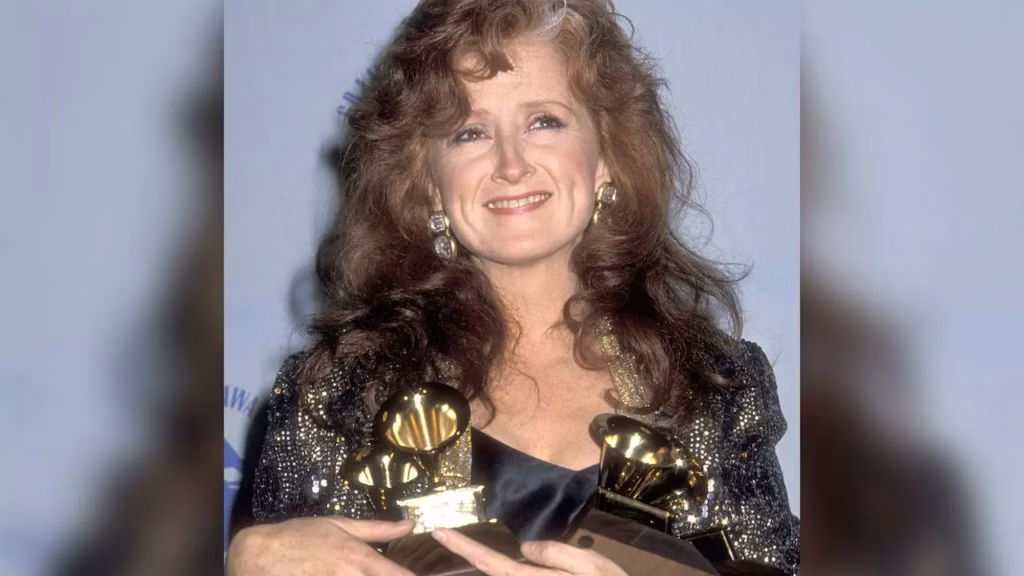 Bonnie Raitt smiles while holding four GRAMMYs