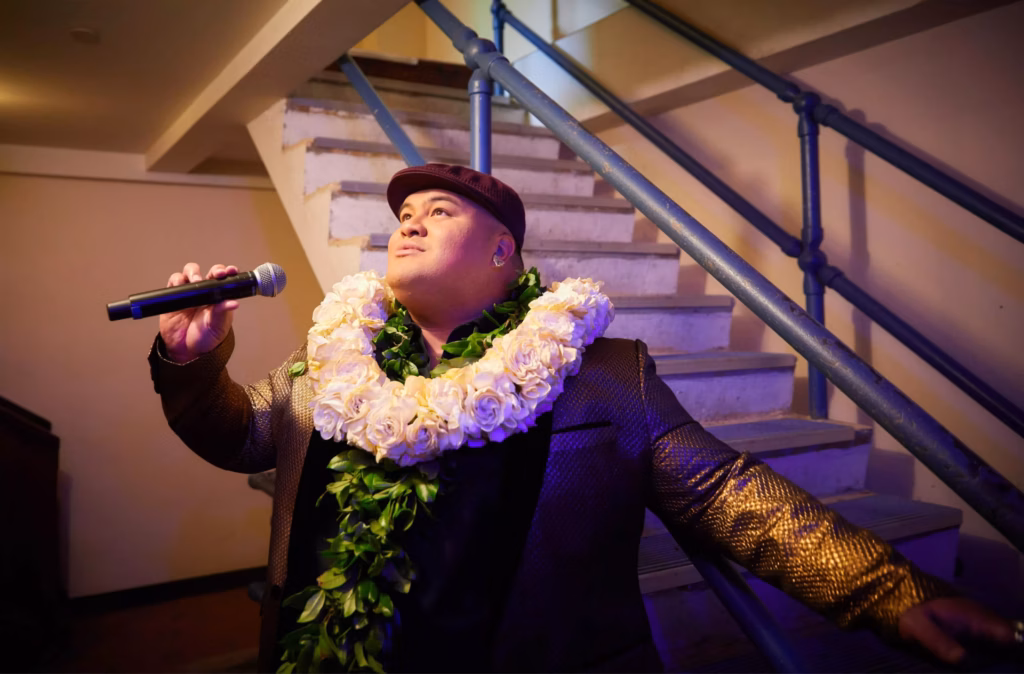 Kalani Pe'a looks up as he sings with a white rose lei