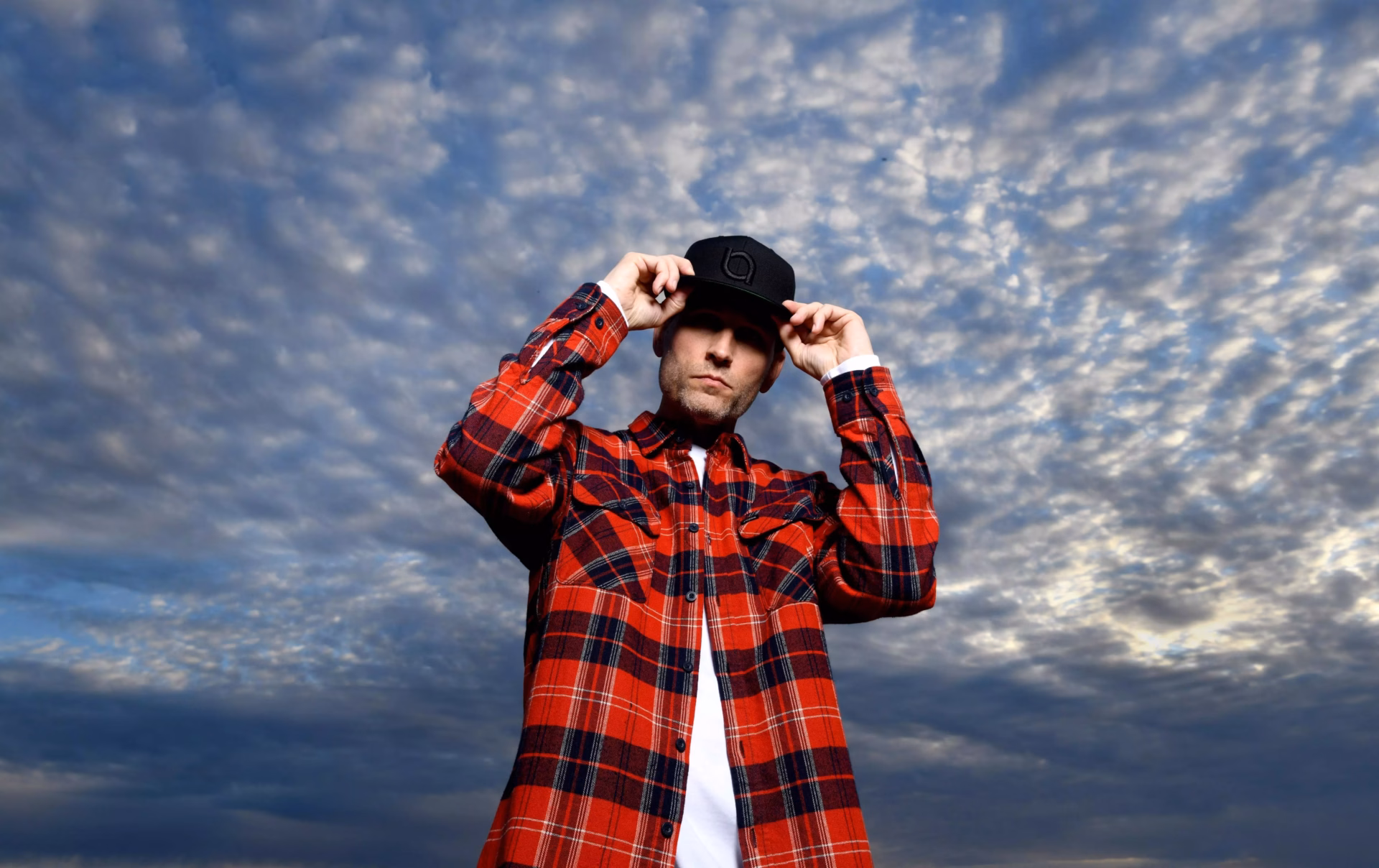 Kaskade stands in front of a cloudy blue sky