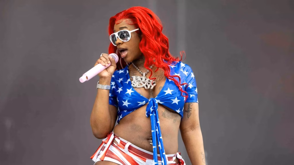 Photo of Sexyy Red performing onstage during at the 2024 Rolling Loud Festival in Los Angeles. She is wearing a blue bikini top with white stars, red and white shorts, white sunglasses, and bright red hair.